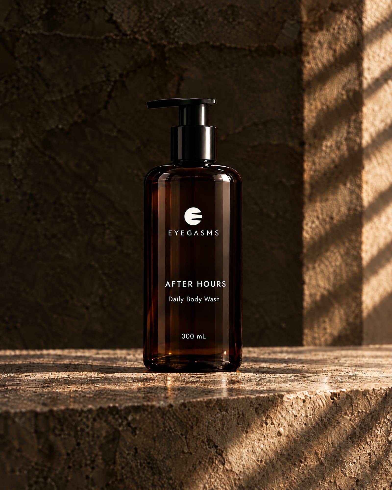 After Hours, daily body wash, by EYEGASMS: an amber bottle with a black pump, 300 mL, alone on a travertine ledge in raking golden light.
