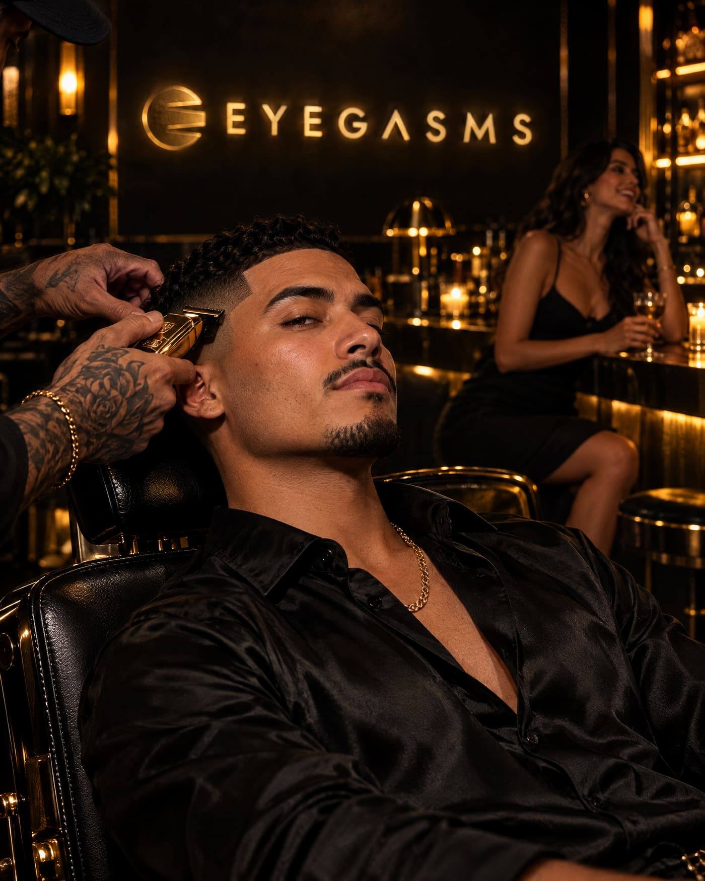 A Latino man leans back in a black leather chair as a barber's tattooed hands finish his taper with a gold clipper; a woman laughs at the bar behind him.